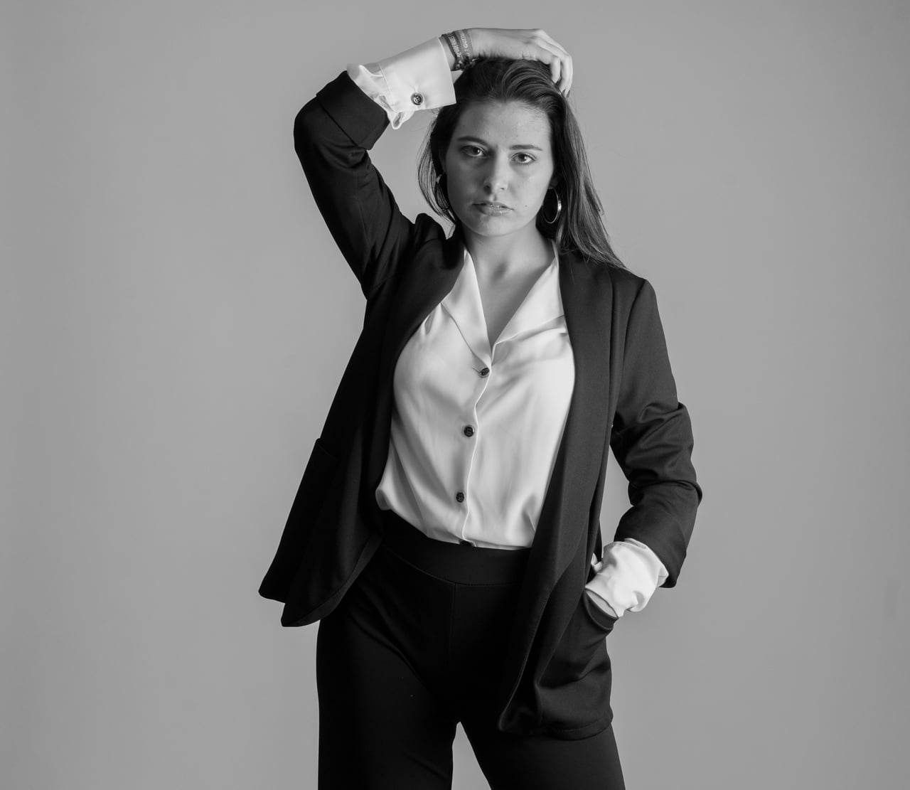 Dona jove amb vestit negre i camisa blanca dempeus, una mà recolzada al cap, retrat en blanc i negre sobre fons d'estudi clar.