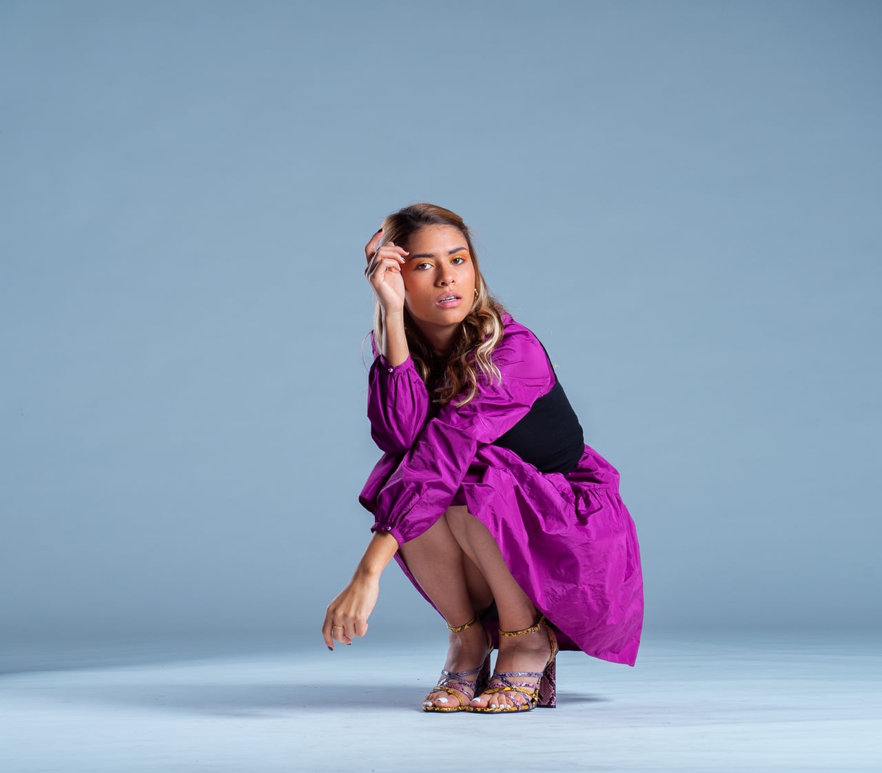 La Bianca Díaz posa en gatzoneta amb una mà recolzada al front en una composició editorial de cos sencer, lluint un vestit curt fúcsia de mànigues bufades, banda ampla negra a la cintura i sandàlies de taló estampades, sobre fons d'estudi blau.