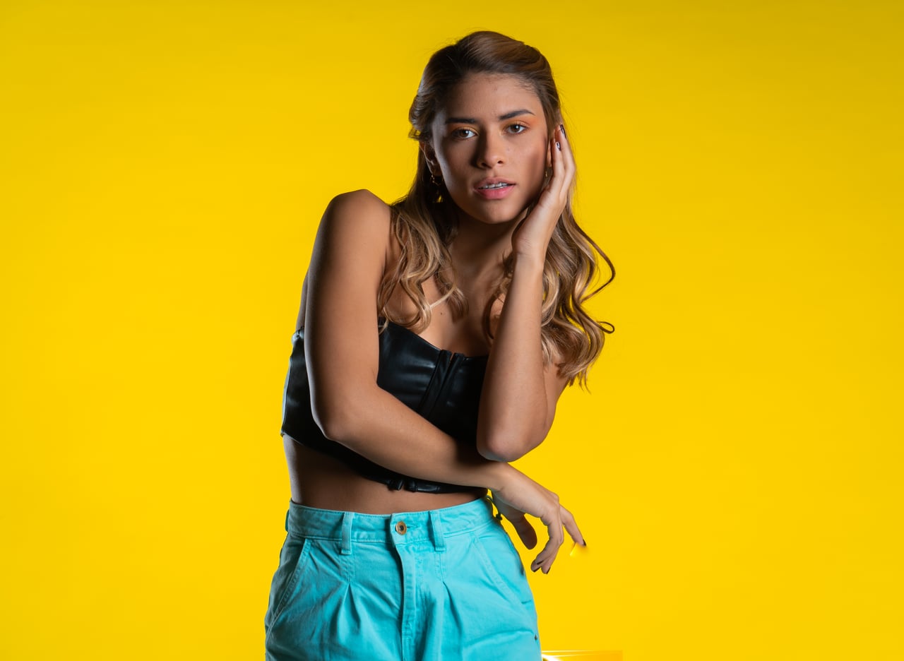 La Bianca Díaz posa de mig cos decantada cap a un costat, amb una mà recolzada a la galta i el braç creuat al davant en un gest editorial, vestida amb top de cotilla de cuir negre i pantaló ample turquesa, davant d'un fons d'estudi groc.