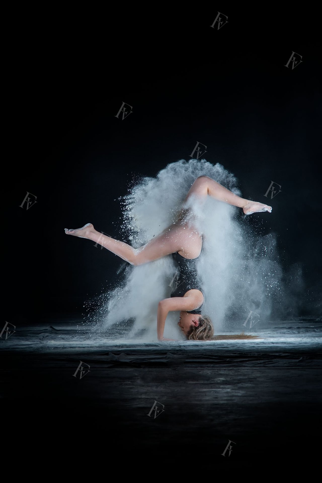 Ballarina amb leotard en pose editorial amb farina blanca volant, fons d'estudi negre.