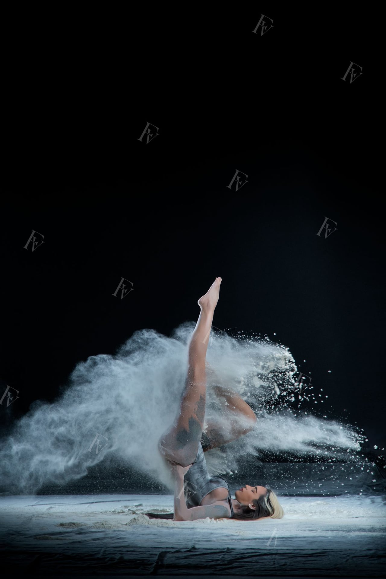 Ballarina amb leotard i cabell llarg en pose dinàmica amb farina blanca, fons d'estudi negre.