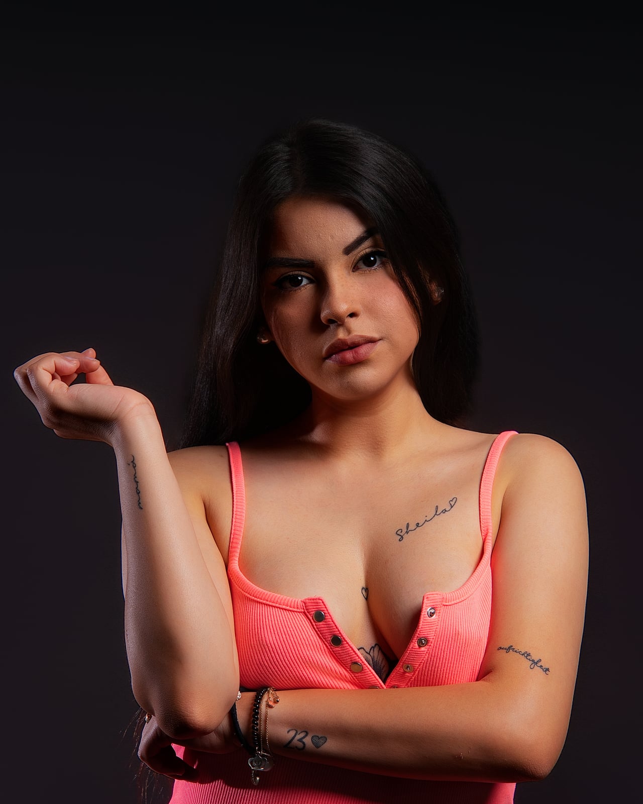 Dona jove amb top neó rosa en pose editorial, fons d'estudi negre low-key.