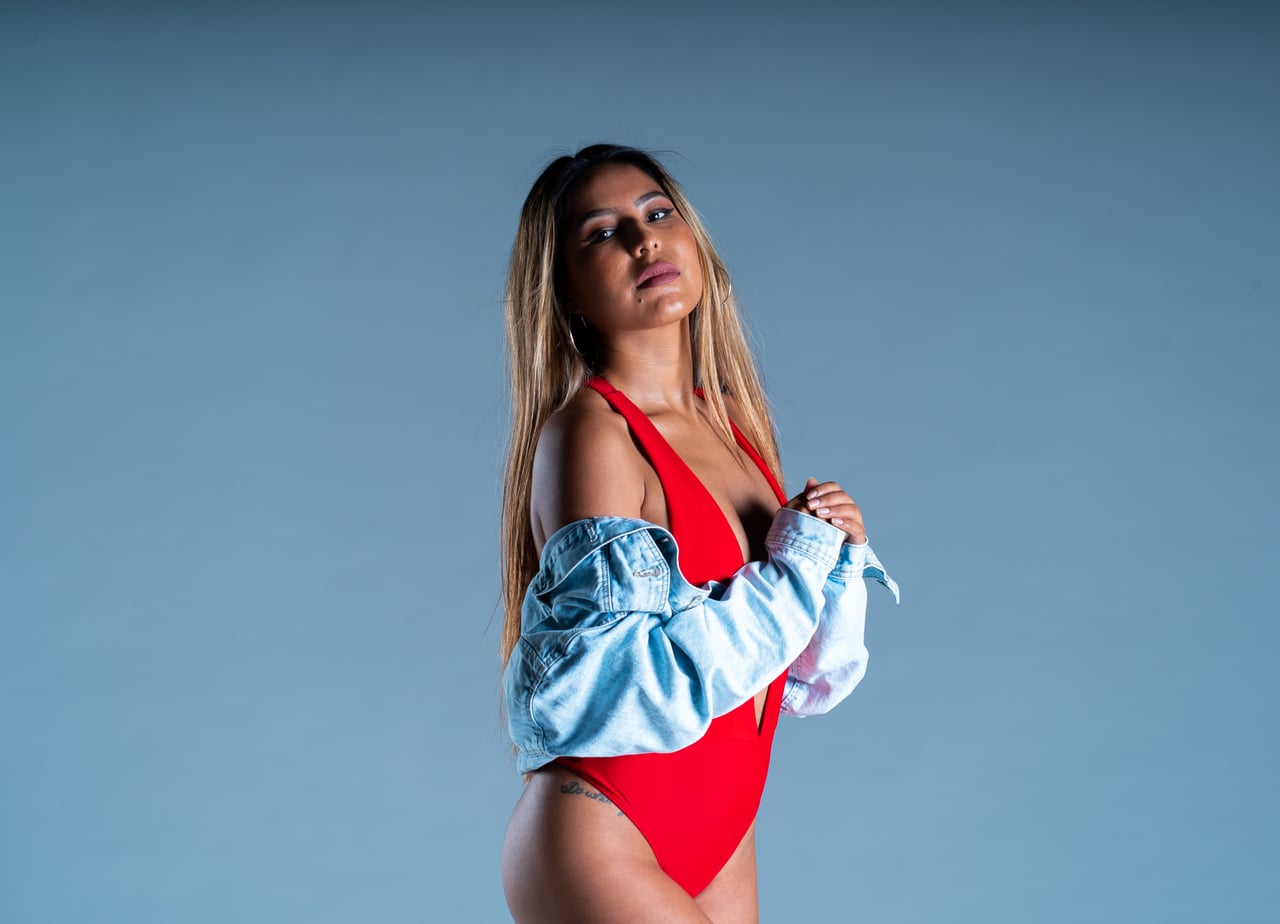 Dona jove amb body vermell i jaqueta texana en pose editorial, fons d'estudi gris blavós.