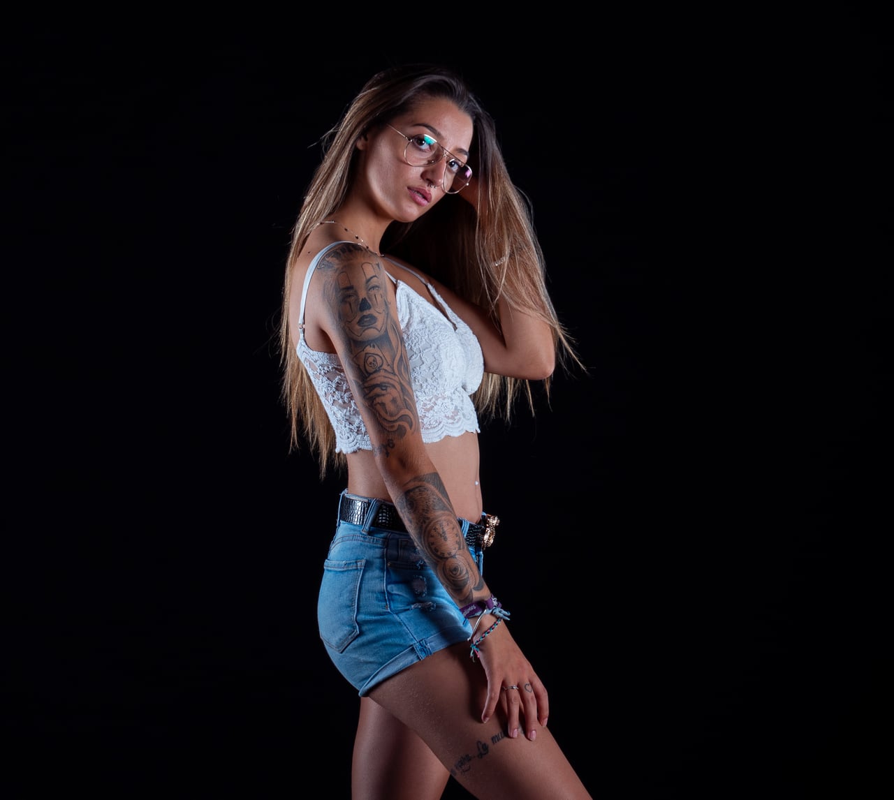 Dona rossa amb top blanc de puntes i pantalons curts texans en pose editorial, fons d'estudi negre.