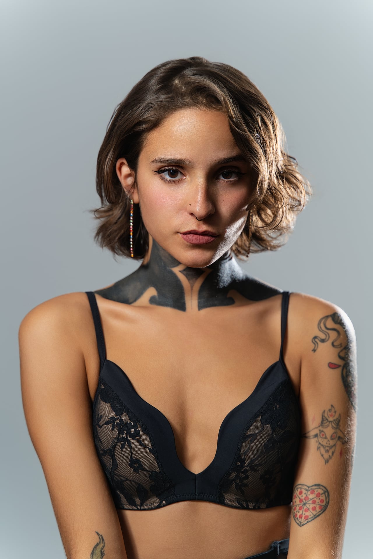 La Rosa posa de mig cos sobre un fons gris llis, amb bralet de puntes negre i tatuatge al coll, una mà a prop del rostre i la mirada a la càmera, amb llum natural suau.